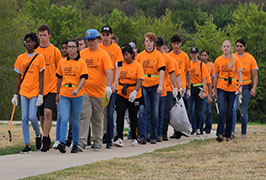 Students in orange shirts walking with trash bags 